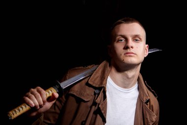 Genç adam bir kahverengi ceket ve beyaz t-shiert, bir katana tutan giymiş. Modern samuria. Moda portre. Kentsel warior. Dramatik ışık