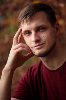 Bir gencin dramatik portresi. Yakın plan. Modaya uygun saç stili ve erkeksi kıllar. Sonbahar mavisi arkaplan