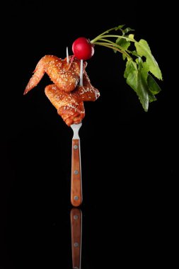 Kızarmış bufalo tavuk kanadı ve turp. Çatala tutturulmuş. Siyah arka planda.