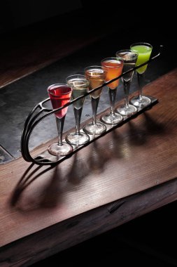 Ahşap masadaki shot bardaklarında renkli alkollü kokteyller.