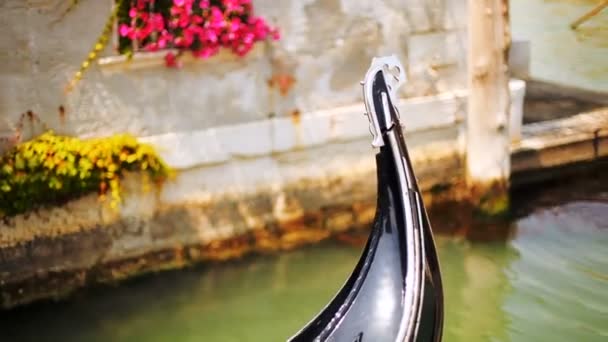 Wenecja. Gondola. Nos ferro gondola. Gondola w kanale w pobliżu starych murów domu z kwiatami. — Wideo stockowe