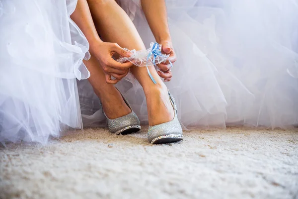 Belle scarpe lucide in piedi di fronte a un bouquet. Chiamate scarpe d'argento. Scarpe da sposa stiletti da sposa ornati con pietre preziose. Sposa in abito da sposa scarpe e giarrettiera . Immagine Stock