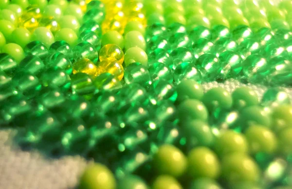 background of green shiny beads. texture of the same green beads. beadwork. seamless pattern of beaded knitting