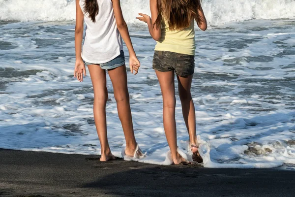 Nice legs of a pretty girl in jeans shorts standing in water. Close-up view of girls\'s legs on the beach