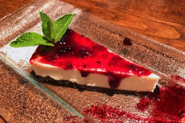 Dilim cheesecake ile kızılcık jam nane yaprağı ile dekore edilmiş cam plaka üzerinde