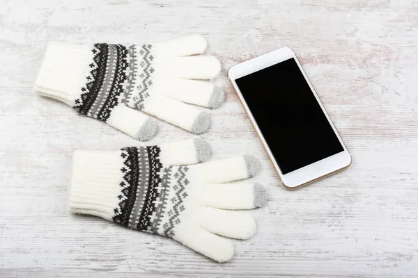 Winterhandschuhe und Smartphone mit leerem Bildschirm auf weißem Holzhintergrund. Smartphone-Attrappe mit leerem schwarzen Bildschirm — Stockfoto