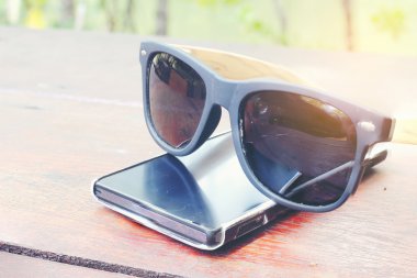 Smartphone ve ahşap masa üzerinde güneş gözlüğü.