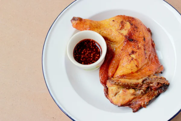 ahşap arka plan üzerinde küçük Kupası'nda baharatlı sos ile beyaz tabakta tavuk budu ızgara. yakın çekim. üstten yatay görünüm.