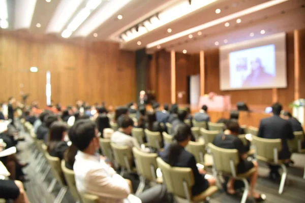 Wazig beeld van onderwijs mensen en mensen uit het bedrijfsleven zitten in de conferentiezaal voor beroep seminar en de spreker is de presentatie van nieuwe technologie en idee te delen met de inhoud activiteit. — Stockfoto