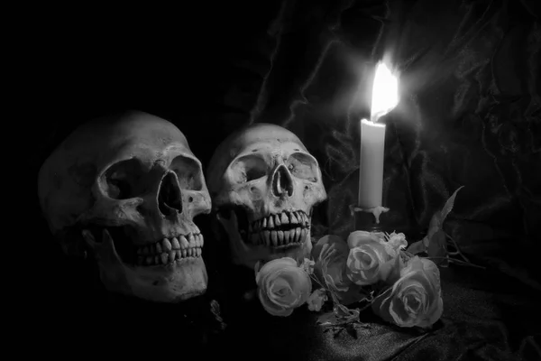 Череп з букетом квітів і свічковим світлом на дерев'яному столі з чорним тлом в нічний час в чорно-білому/ Стиль життя — стокове фото