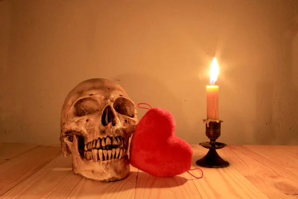 Crânio humano e corações vermelhos com vela de luz na mesa de madeira à noite, fotografia ainda luz . — Fotografia de Stock