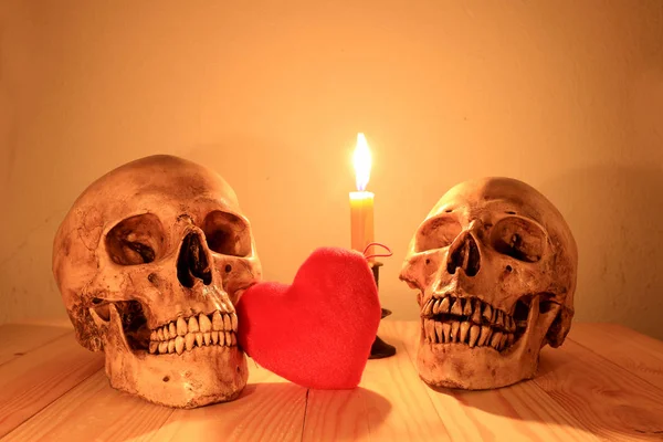 Crânio humano e corações vermelhos com vela de luz na mesa de madeira à noite, fotografia ainda luz . — Fotografia de Stock