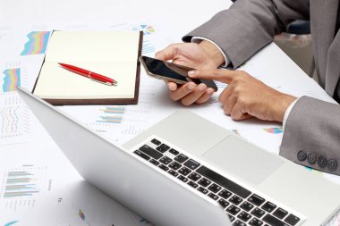 adam eller iş Ofis Masası cep telefonu, dizüstü bilgisayar, kalem ve defter kullanarak meşgul. Analiz Çizelgeler ve grafikler onların başarılı ekip çalışması sonuçlar. İş kavramı