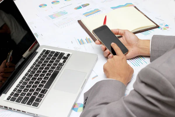 Homem de negócios mãos ocupadas usando telefone celular, laptop, caneta e notebook na mesa de escritório. Analise os gráficos e gráficos que mostram os resultados de seu trabalho em equipe bem sucedido. Conceito de negócio — Fotografia de Stock