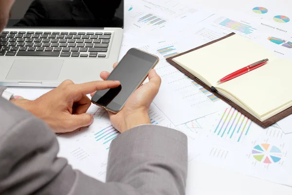 Homem de negócios mãos ocupadas usando telefone celular, laptop, caneta e notebook na mesa de escritório. Analise os gráficos e gráficos que mostram os resultados de seu trabalho em equipe bem sucedido. Conceito de negócio — Fotografia de Stock