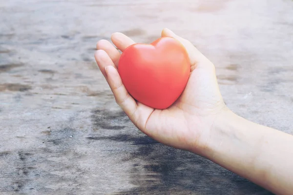 Female hands giving red heart overhead of wooden planks in the morning light. Filtered color. vintage tone. — Stock Photo, Image