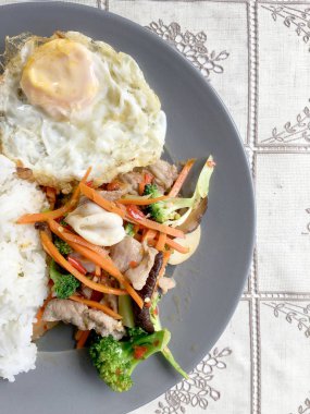 Sote karışık sebze n istiridye soslu pilav ve kızarmış yumurta beyaz tabakta. Tayland gıda.