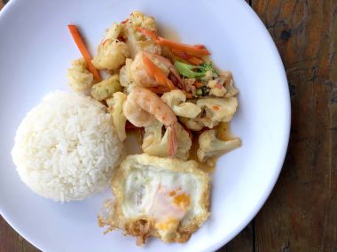 fasulye ve pilav ve kızarmış yumurta ahşap arka plan üzerinde beyaz tabak karides sebzeler ile tavada. Tay tarzında gıda.