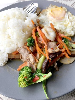 Sote karışık sebze n istiridye soslu pilav ve kızarmış yumurta beyaz tabakta. Tayland gıda.