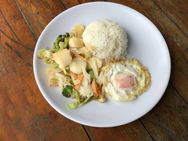 Tofu ve ahşap arka plan üzerinde beyaz tabak pirinç kızarmış yumurta ile tavada kızartılmış karışık sebze. Vejetaryen yiyecekler, sağlıklı gıda.