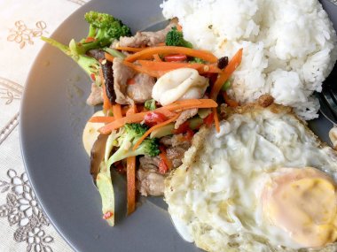 Sote karışık sebze n istiridye soslu pilav ve kızarmış yumurta beyaz tabakta. Tayland gıda.