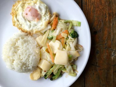 Tofu ve ahşap arka plan üzerinde beyaz tabak pirinç kızarmış yumurta ile tavada kızartılmış karışık sebze. Vejetaryen yiyecekler, sağlıklı gıda.