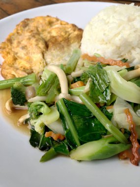 Kızarmış sebze Tay omlet (yumurta) ile pirinç rustik ahşap arka plan üzerinde beyaz plaka ile karıştırın. Vejetaryen yiyecekler, sağlıklı gıda.