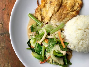 Kızarmış sebze Tay omlet (yumurta) ile pirinç rustik ahşap arka plan üzerinde beyaz plaka ile karıştırın. Vejetaryen yiyecekler, sağlıklı gıda.