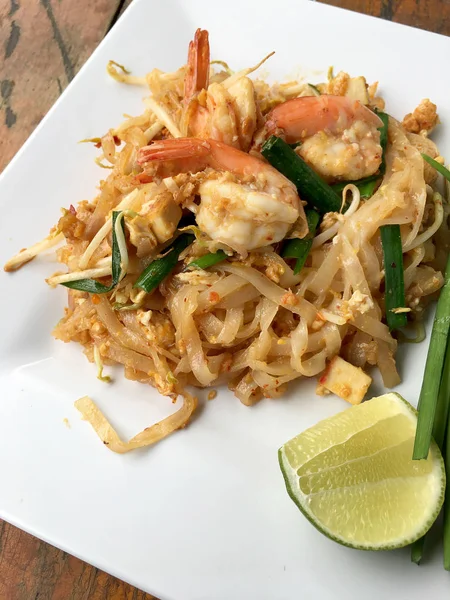 Thai gebratene Nudeln "pad thai" mit Garnelen und Gemüse in weißem Teller auf Holzgrund. das thailändische Nationalgericht. das beliebte essen in thailand. Thailändische gebratene Nudeln. — Stockfoto