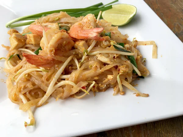 Thajské smažené nudle "Pad Thai" s krevetami a zeleninou v bílé desky na dřevěných pozadí. Ten thajský národní hlavní jídlo. oblíbené jídlo v Thajsku. Smažené thajské nudle. — Stock fotografie