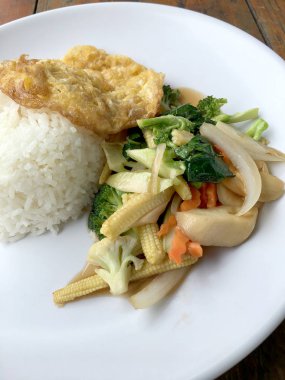 Ahşap arka plan beyaz bir tabağa omlet ile kızartma sebze ilave edin. Tay tarzı yiyecek. Vejetaryen yiyecekler