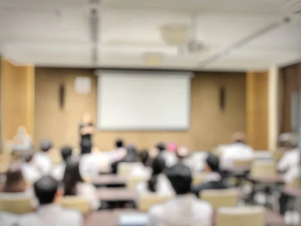 Abstract blurred background image of students and business people studying and discuss in large hall profession seminar with screen and projector for showing information.