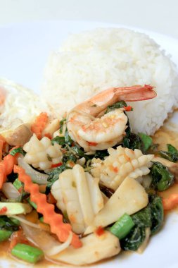 Asya gıda, kızarmış heyecan chili Yapıştır ile deniz ürünleri ve pirinç beyaz tabakta, baharatlı sıcak biber Tayland yemekleri ile fesleğen yaprakları.