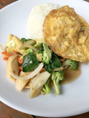 Ahşap arka plan beyaz bir tabağa omlet ile kızartma sebze ilave edin. Tay tarzı yiyecek. Vejetaryen yiyecekler