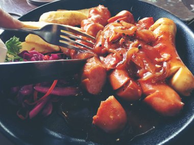 Sarımsak, otlar ve patates kızartması bir tavada kızarmış sosis.