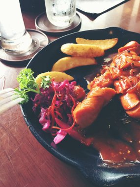 Sarımsak, otlar ve patates kızartması bir tavada kızarmış sosis.