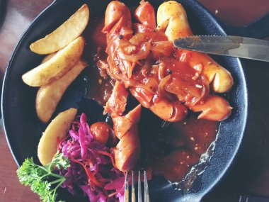 Sarımsak, otlar ve patates kızartması bir tavada kızarmış sosis.