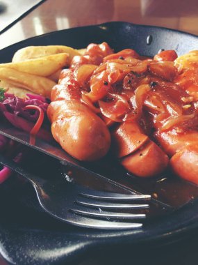 Sarımsak, otlar ve patates kızartması bir tavada kızarmış sosis