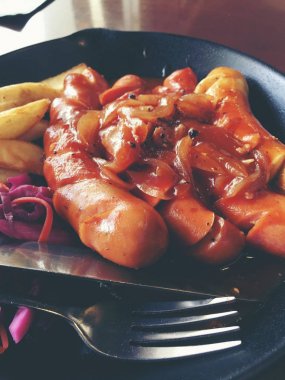 Sarımsak, otlar ve patates kızartması bir tavada kızarmış sosis