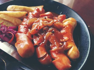 Sarımsak, otlar ve patates kızartması bir tavada kızarmış sosis