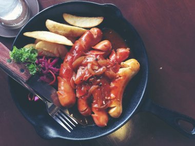 Sarımsak, otlar ve patates kızartması bir tavada kızarmış sosis