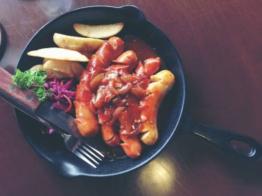 Sarımsak, otlar ve patates kızartması bir tavada kızarmış sosis