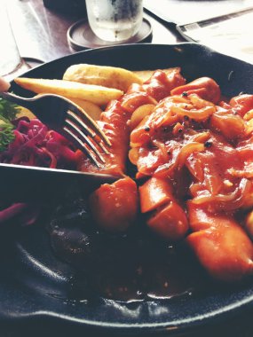 Sarımsak, otlar ve patates kızartması bir tavada kızarmış sosis