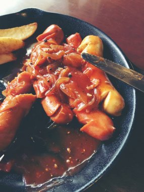 Sarımsak, otlar ve patates kızartması bir tavada kızarmış sosis