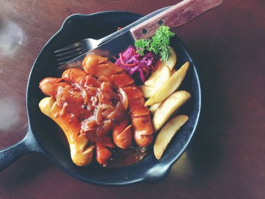 Sarımsak, otlar ve patates kızartması bir tavada kızarmış sosis