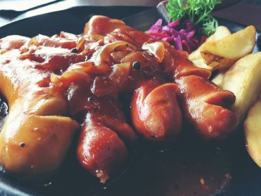 Sarımsak, otlar ve patates kızartması bir tavada kızarmış sosis