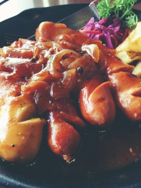 Sarımsak, otlar ve patates kızartması bir tavada kızarmış sosis