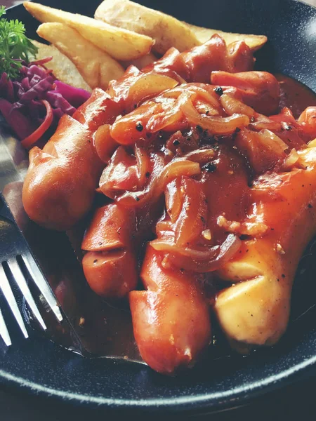 Salsichas fritas com alho, ervas e batatas fritas em uma panela . — Fotografia de Stock