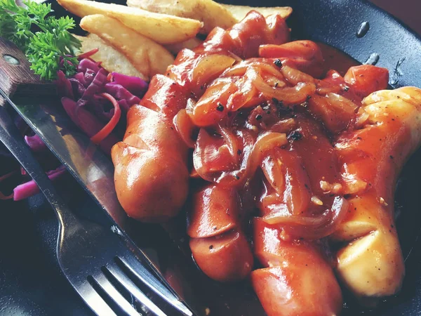 Salsichas fritas com alho, ervas e batatas fritas em uma panela . — Fotografia de Stock