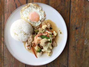 Kızarmış sebze, karnabahar, havuç, pirinç ve ahşap arka plan üzerinde beyaz tabak içinde kızarmış yumurta ile deniz ürünleri ile şeker bezelye karışımı. Tay tarzında gıda.